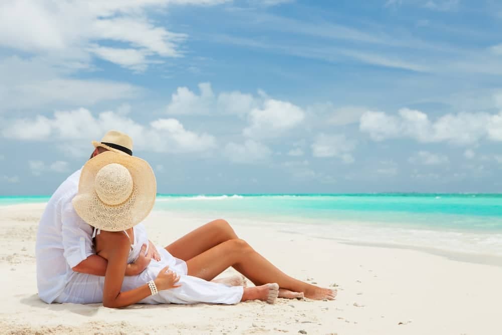 couple-sitting-on-beach-tropical-island-honeymoon-ocean-summer-shutterstock_151787042