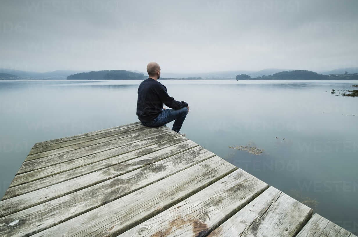 lonely-man-sitting-on-jetty-looking-at-distance-RAEF02179